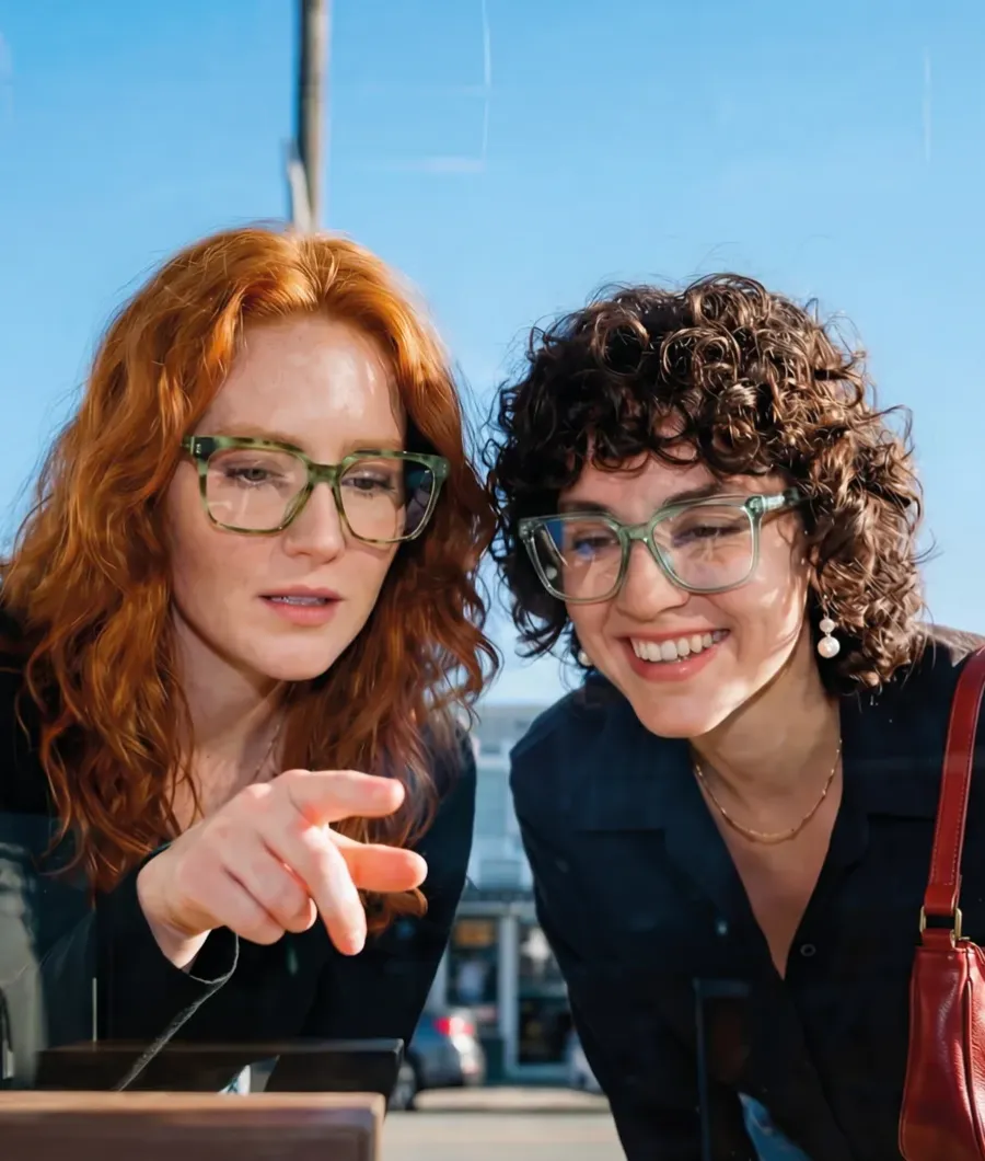 Brillen Closeup aktivoptik - Zwei Frauen mit Brille stehen vor einem Schaufenster und eine zeigt mit dem Fingre auf eine Brillenfassung