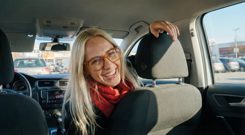Service aktivoptik - Frau mit Brille und rotem Schal lacht während sie vorne im Auto sitzt und dreht sich nach hinten zur Rückbank