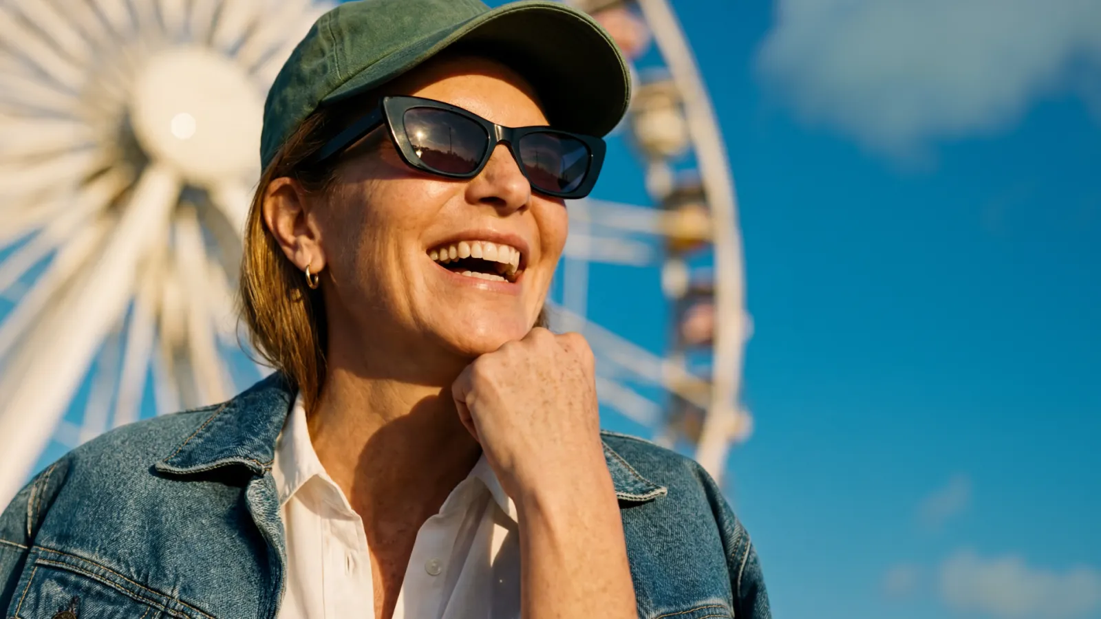 Sonnenbrillen aktivoptik - Frau mit Sonnenbrille und Cap lächelt mit  abgestzützem Kinn vor einem Riesenrad